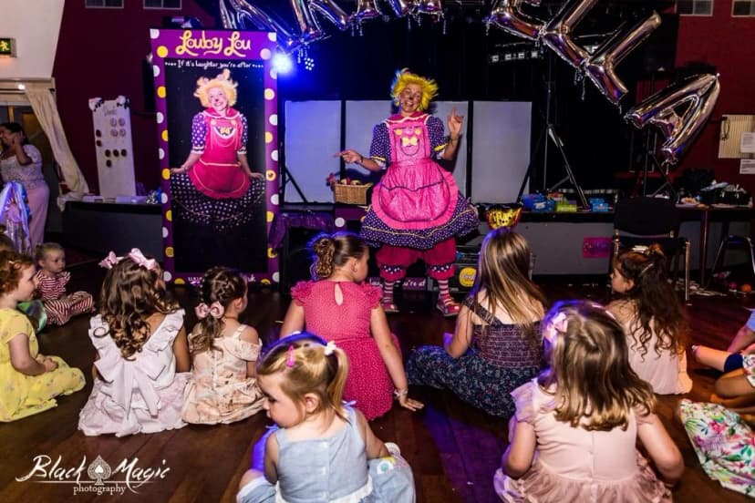 This is an image showing Louby Lou the female clown performing an interactive clown performance complete with comedy and magic for kids at a fun party event. She is dancing for the children in her clown attire.