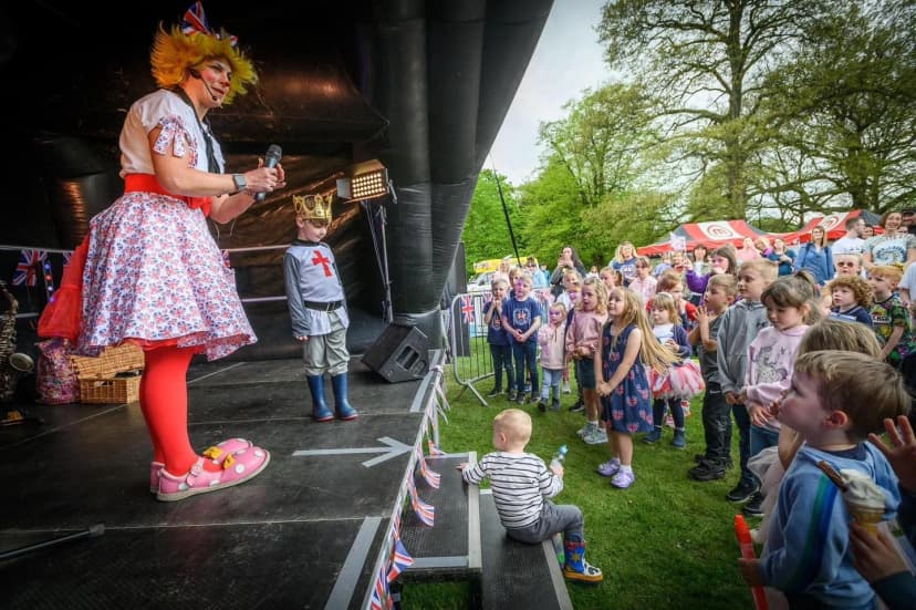 An image of Louby Lou, the clown, on top of a stage, performing to a large crowd of children. There's plenty of giggles on display, from both Louby Lou and the Children. This image was taken in Greater Manchester